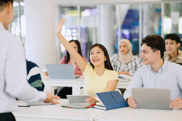 happy  student raising arm to answer question while attending class with her university colleagues. - 教育 個照片及圖片檔